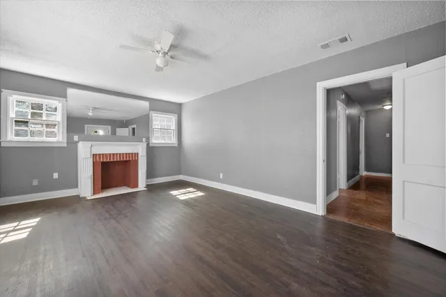 an empty room with wooden floor a ceiling fan and a kitchen