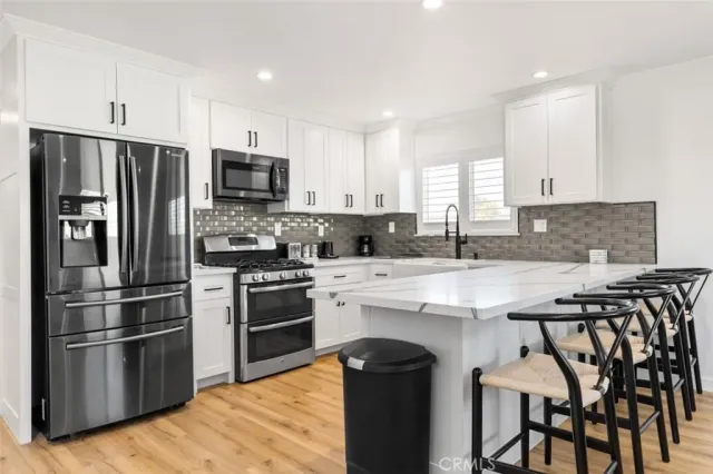 a kitchen with stainless steel appliances granite countertop a stove a sink a microwave a refrigerator and white cabinets