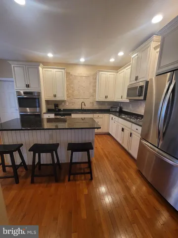 a kitchen with stainless steel appliances granite countertop a stove top oven a sink a dining table and chairs with wooden floor