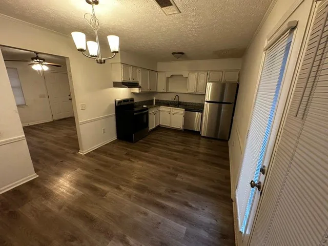 a kitchen with stainless steel appliances granite countertop a refrigerator a sink dishwasher a stove and white countertops with wooden floor