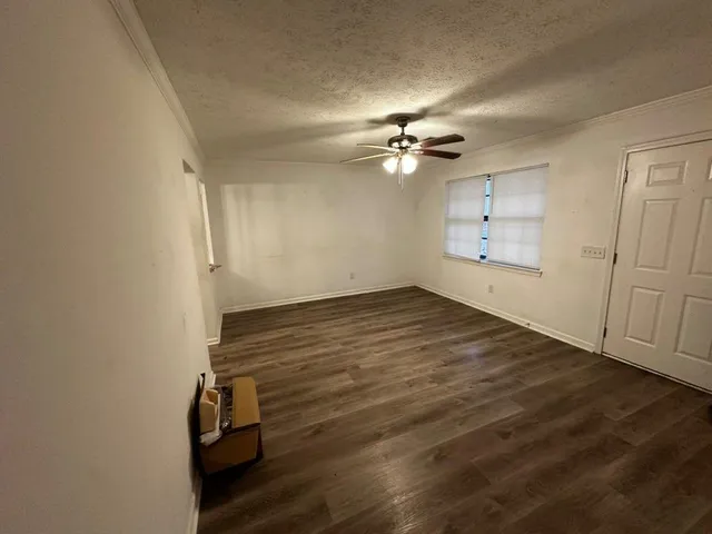 an empty room with wooden floor chandelier fan and windows