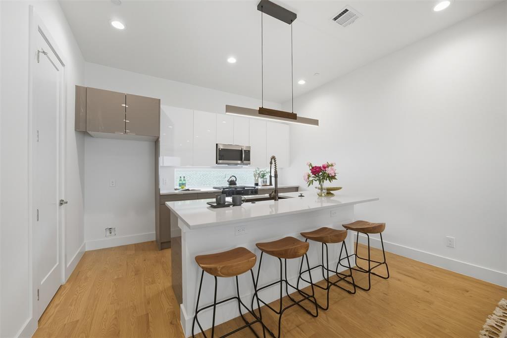 4517 Munger Avenue, Unit 101 Dallas, TX 75204 - Photo 27 of 39 a kitchen with stainless steel appliances a stove a sink refrigerator and a dining table with wooden floor