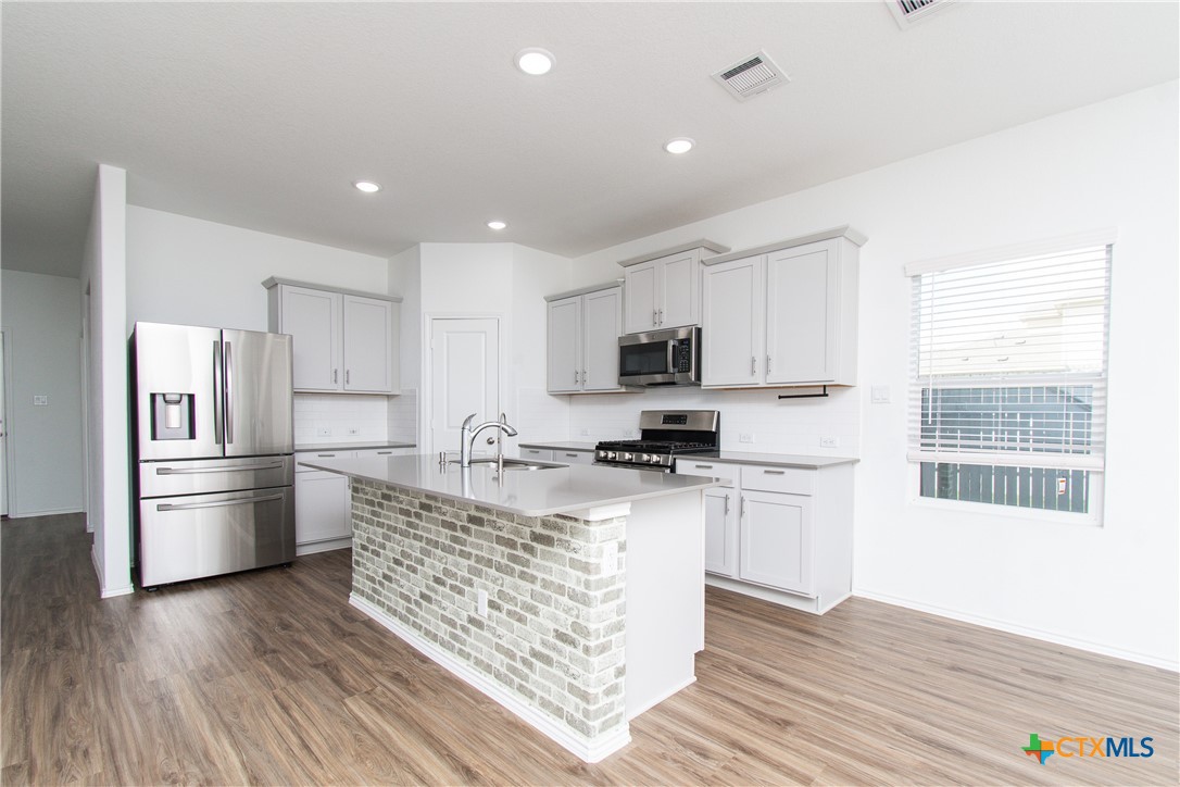 9101 Daisy Cutter Crossing Georgetown, TX 78626 - Photo 4 of 28 a kitchen with stainless steel appliances kitchen island granite countertop a refrigerator oven a stove top oven and granite counter tops with wooden floors