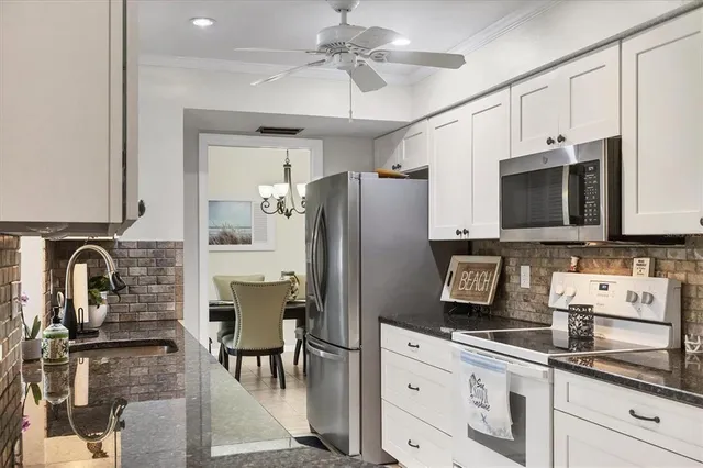 a kitchen with stainless steel appliances granite countertop a refrigerator a stove a sink and white cabinets with wooden floor