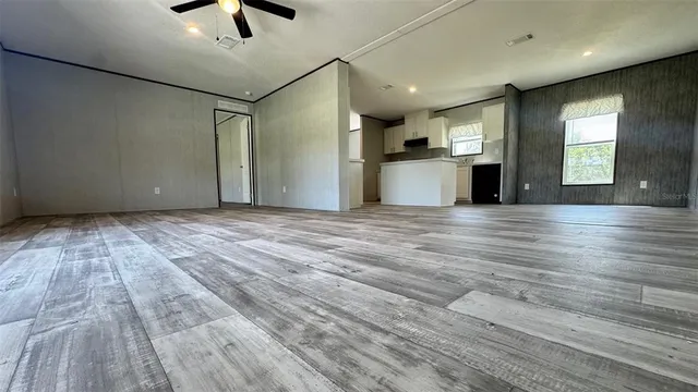 an empty room with wooden floor kitchen view and windows