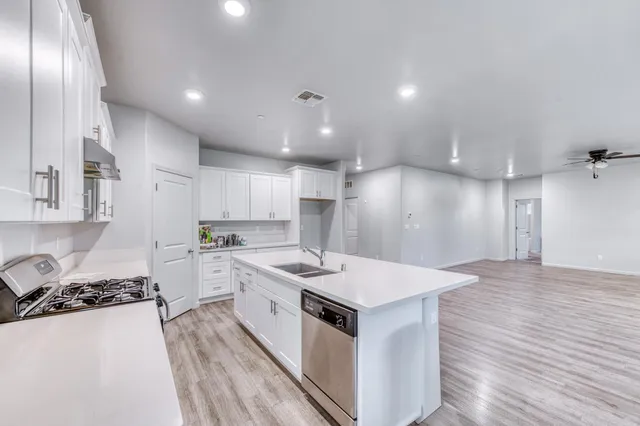 a kitchen with stainless steel appliances granite countertop a stove top oven a sink dishwasher and a refrigerator with wooden floor