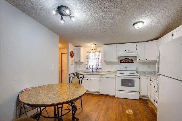 a kitchen with kitchen island a stove a sink a refrigerator and white cabinets with wooden floor