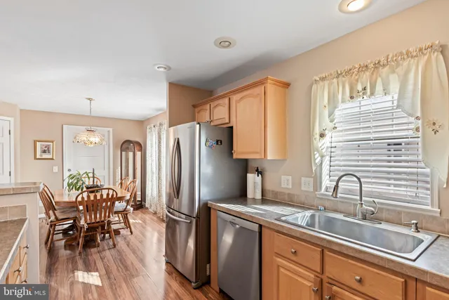 a kitchen with stainless steel appliances granite countertop a refrigerator a sink dishwasher a dining table and chairs with wooden floor