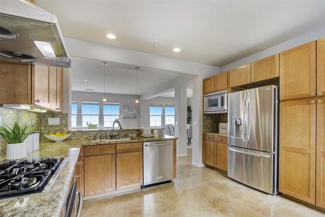 a kitchen with stainless steel appliances granite countertop a refrigerator a stove a sink a dining table and chairs with wooden floor