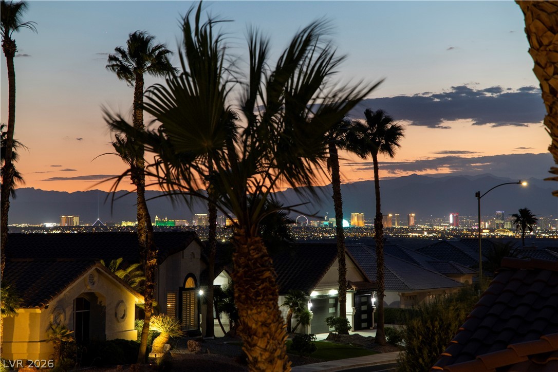 1135 Calico Ridge Drive Henderson, NV 89011 - Photo 78 of 86 Here are the views from the balcony. City lights twinkle across the horizon at dusk, framed by lush palm trees and distant mountains.