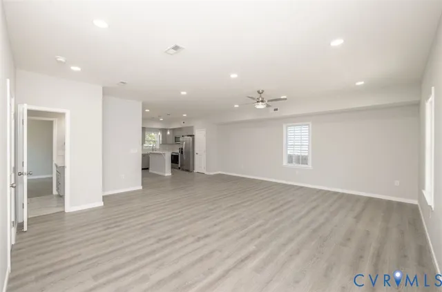 an empty room with wooden floor kitchen and windows