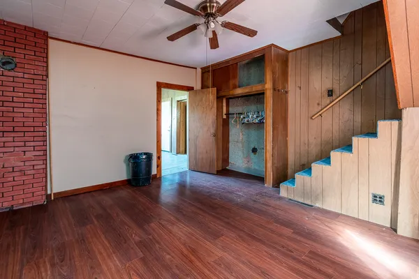 a view of an empty room with wooden floor and a ceiling fan