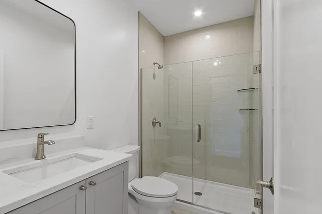 a bathroom with a shower sink vanity mirror and toilet