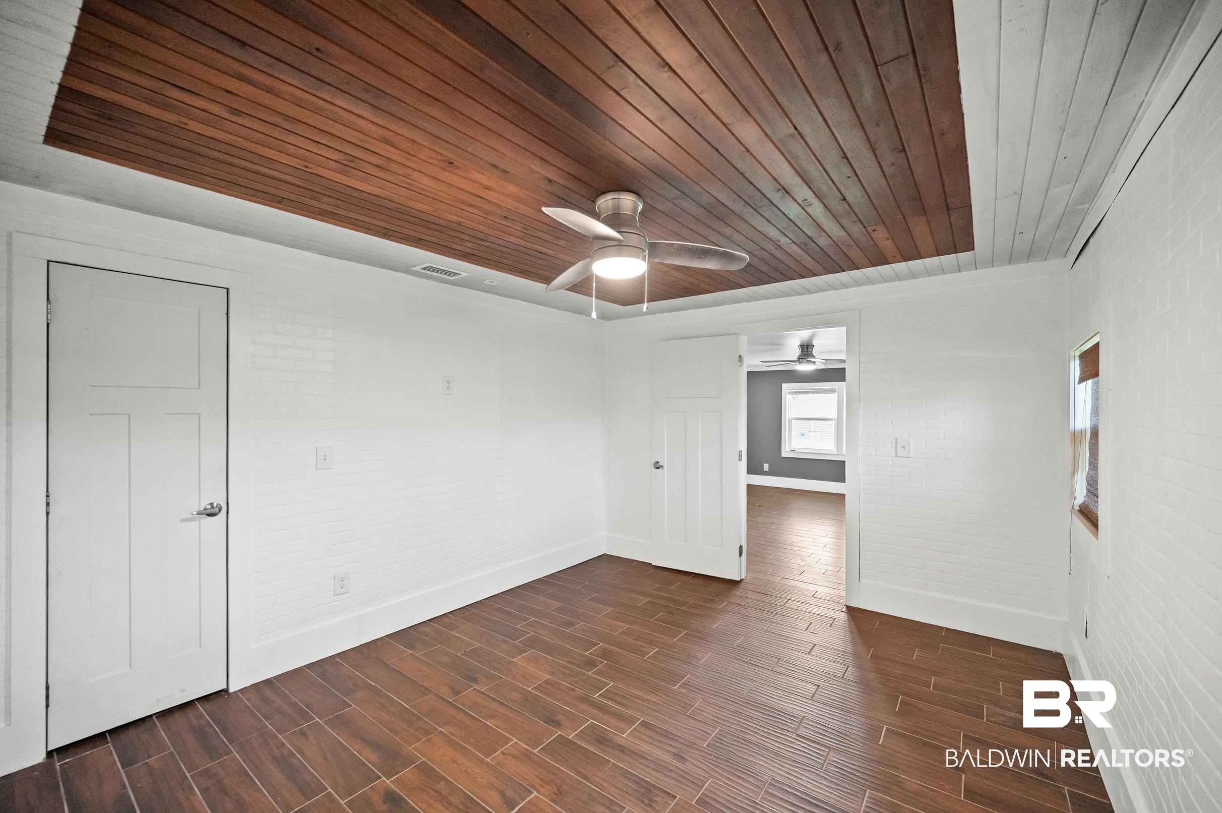 24663 Chestnut Street Elberta, AL 36530 - Photo 10 of 22 Room featuring wood-finish tile flooring, white brick-patterned walls, and a recessed wood-paneled ceiling with a ceiling fan