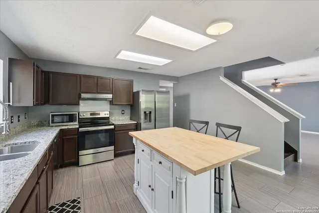 a kitchen with stainless steel appliances a stove a sink dishwasher a refrigerator with white cabinets and wooden floor