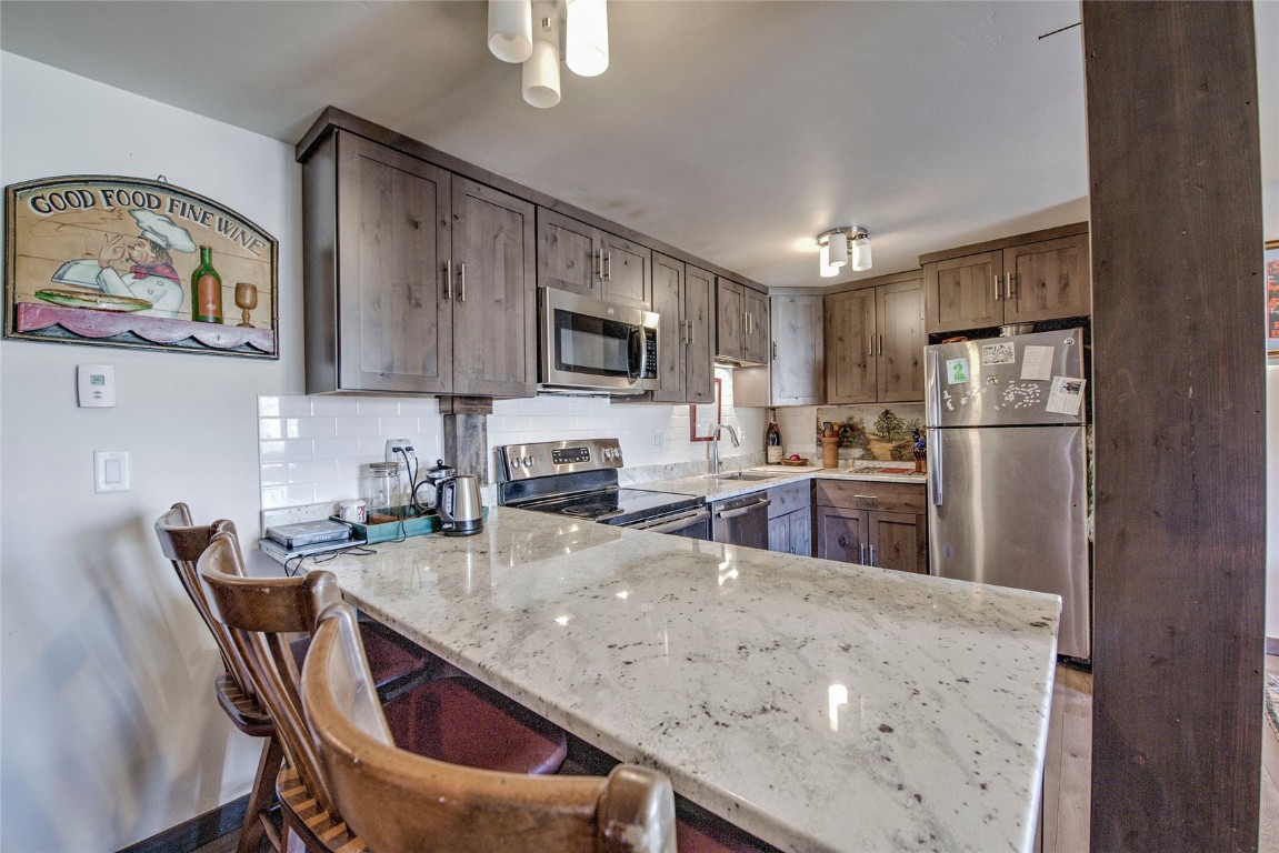 150 Evergreen Road, Unit 106 Dillon, CO 80435 - Photo 17 of 19 a kitchen with stainless steel appliances granite countertop a refrigerator a stove a sink a microwave a dining table and chairs with wooden floor