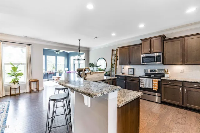 a kitchen with stainless steel appliances granite countertop a stove top oven a sink dishwasher a dining table and chairs with wooden floor