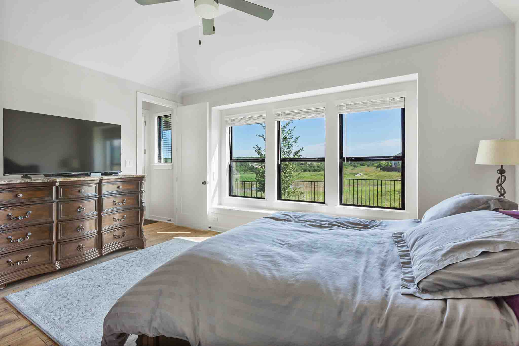 220 Basket Flower Loop Kyle, TX 78640 - Photo 17 of 40 Natural light floods this primary bedroom, highlighting its vaulted ceilings and scenic outdoor views.