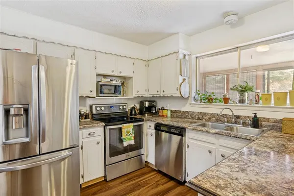 a kitchen with stainless steel appliances granite countertop a refrigerator a stove and white cabinets with wooden floor