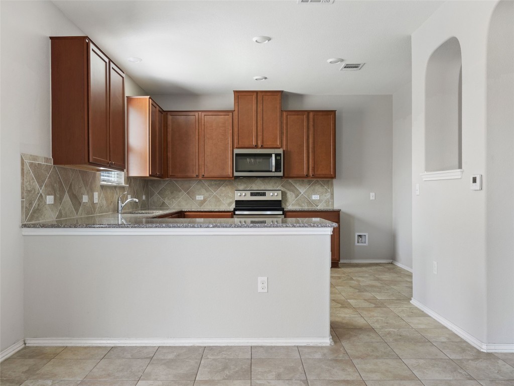 7633 Rio Pass Austin, TX 78724 - Photo 5 of 23 Kitchen with stainless steel appliances, wood finish cabinetry, dark stone countertops, and backsplash
