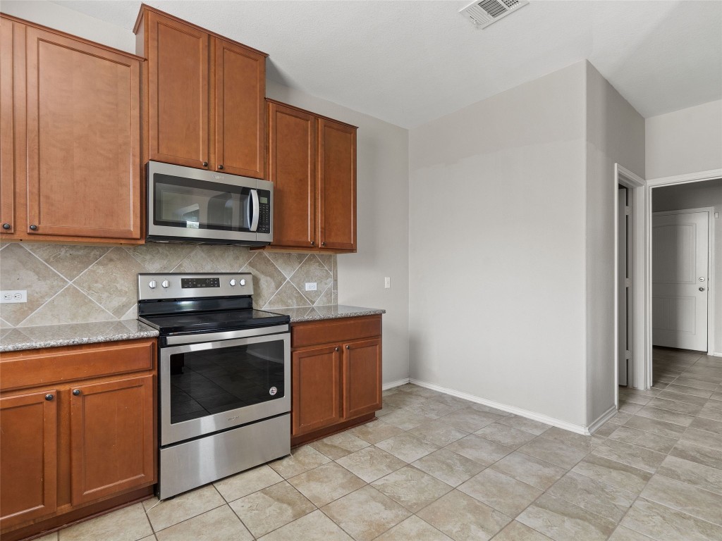 7633 Rio Pass Austin, TX 78724 - Photo 6 of 23 Kitchen with stainless steel appliances, wood finish cabinetry, decorative backsplash, and light stone counters