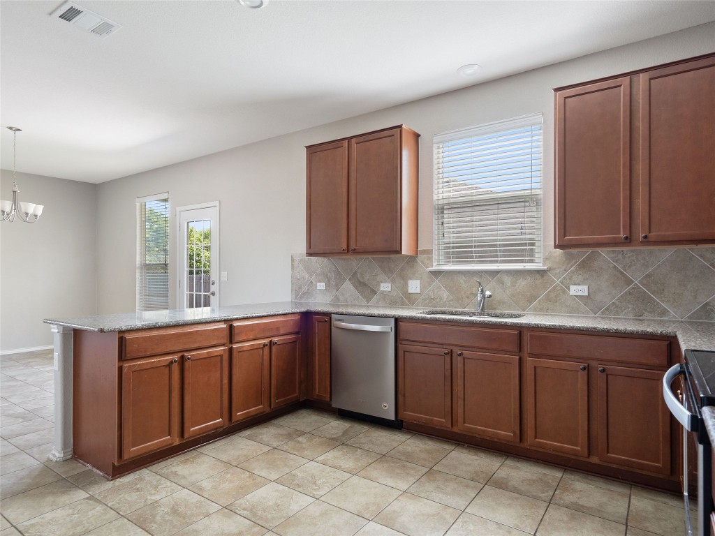 7633 Rio Pass Austin, TX 78724 - Photo 9 of 23 Kitchen with a peninsula, stainless steel appliances, light stone countertops, hanging lights, and wood finish cabinetry