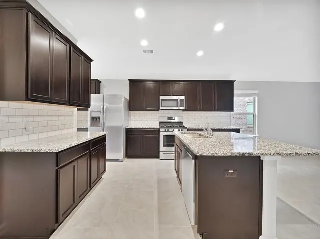 a kitchen with stainless steel appliances kitchen island granite countertop a sink and a stove top oven with wooden floor