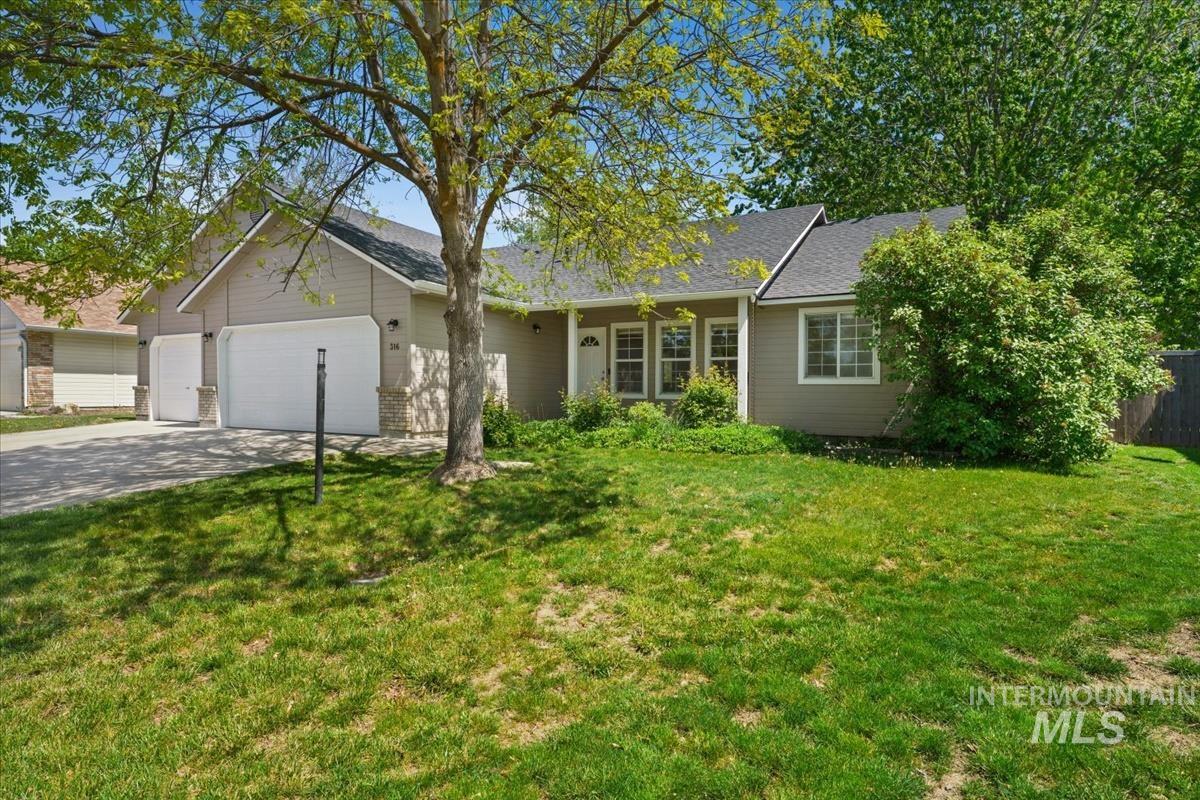 Single-story residence featuring a two-car garage with individual doors, a paved driveway, and a front lawn with mature trees and shrubs