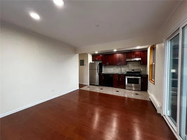 an empty room with wooden floor kitchen view and a fireplace