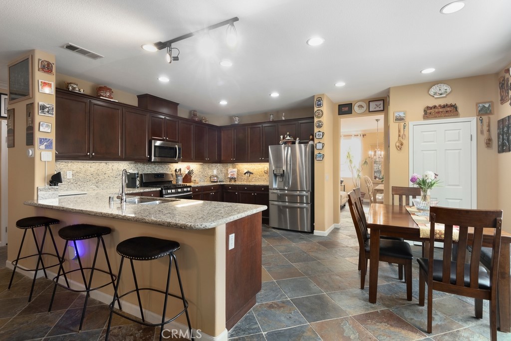 130 Daylily Drive Perris, CA 92571 - Photo 13 of 43 a kitchen with stainless steel appliances kitchen island granite countertop a table chairs and a refrigerator