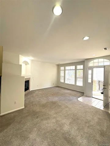 an empty room with windows and view of kitchen