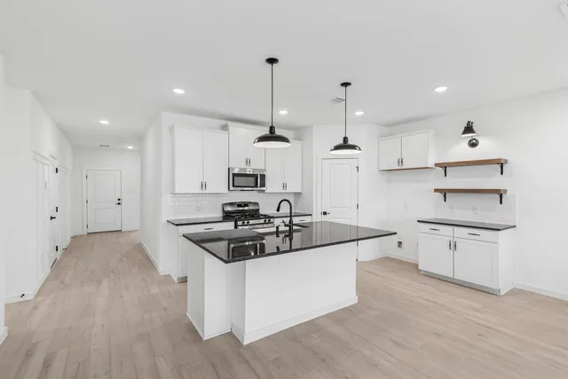 a kitchen with stainless steel appliances kitchen island a stove a sink a refrigerator and white cabinets with wooden floor