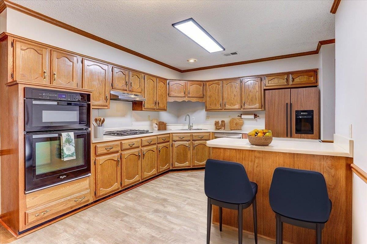 Kitchen featuring crown molding, a kitchen bar, light countertops, a peninsula, and paneled built in refrigerator