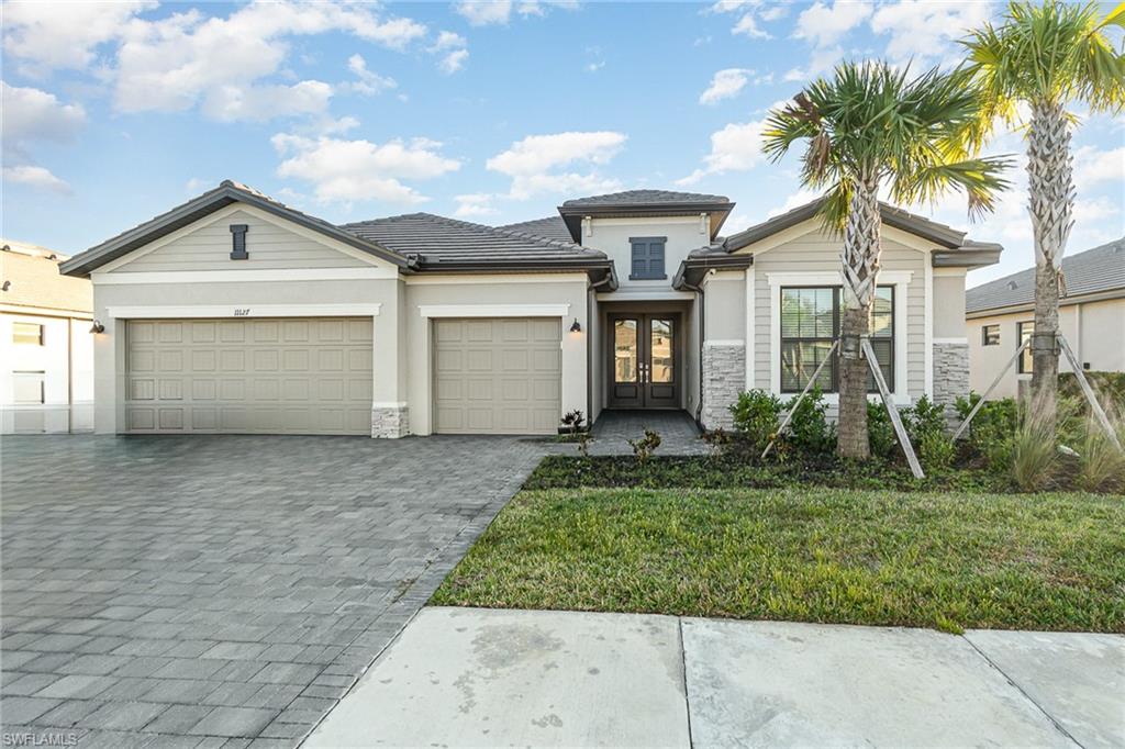 View of front of property featuring decorative driveway, french doors, an attached garage, a front yard, and stucco siding