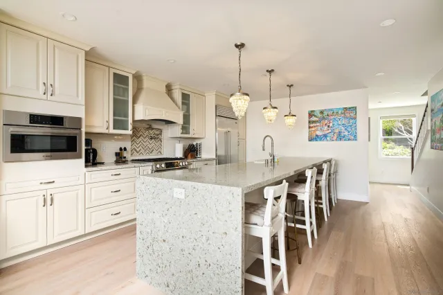 a kitchen with stainless steel appliances kitchen island granite countertop a stove a sink and white cabinets with wooden floor