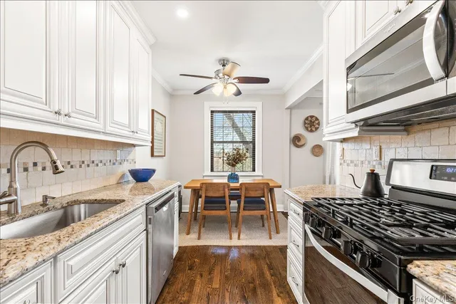 a kitchen with stainless steel appliances granite countertop a stove a sink dishwasher and white cabinets with wooden floor