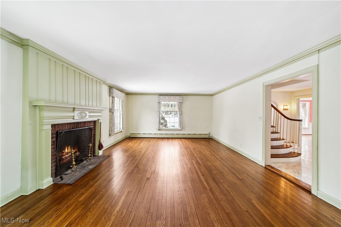 2995 Brighton Road Cleveland, OH 44120 - Photo 10 of 39 Unfurnished living room with wood finished floors, stairs, baseboard heating, a brick fireplace, and crown molding