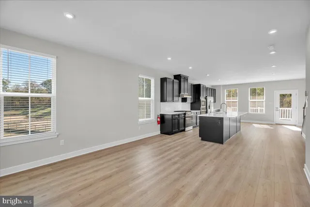 a large white kitchen with kitchen island a sink wooden floor and black appliances