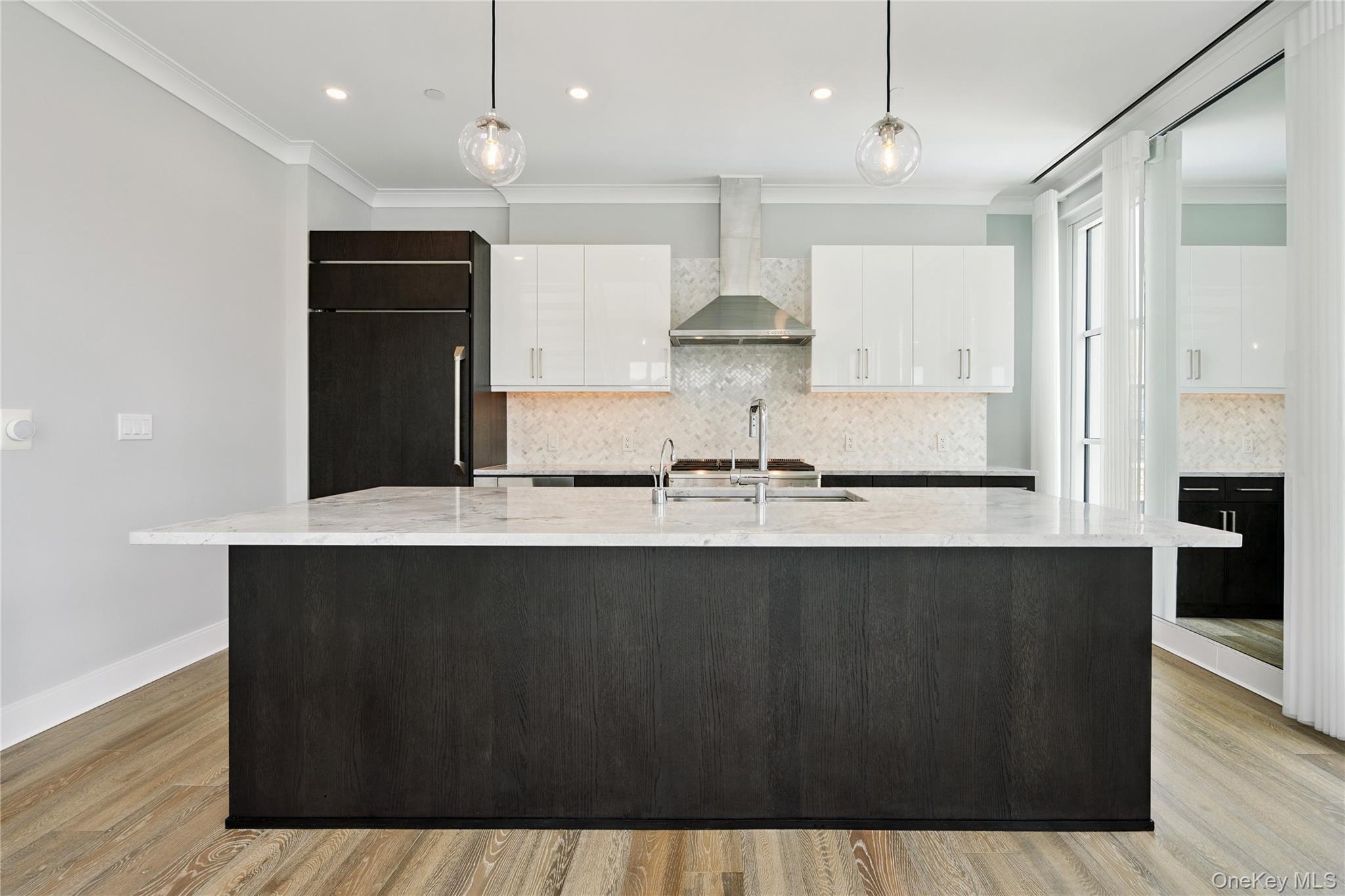100 Garvies Point Road, Unit 1304 Glen Cove, NY 11542 - Photo 11 of 34 Kitchen with white cabinetry, ornamental molding, tasteful backsplash, wall chimney exhaust hood, and light stone countertops