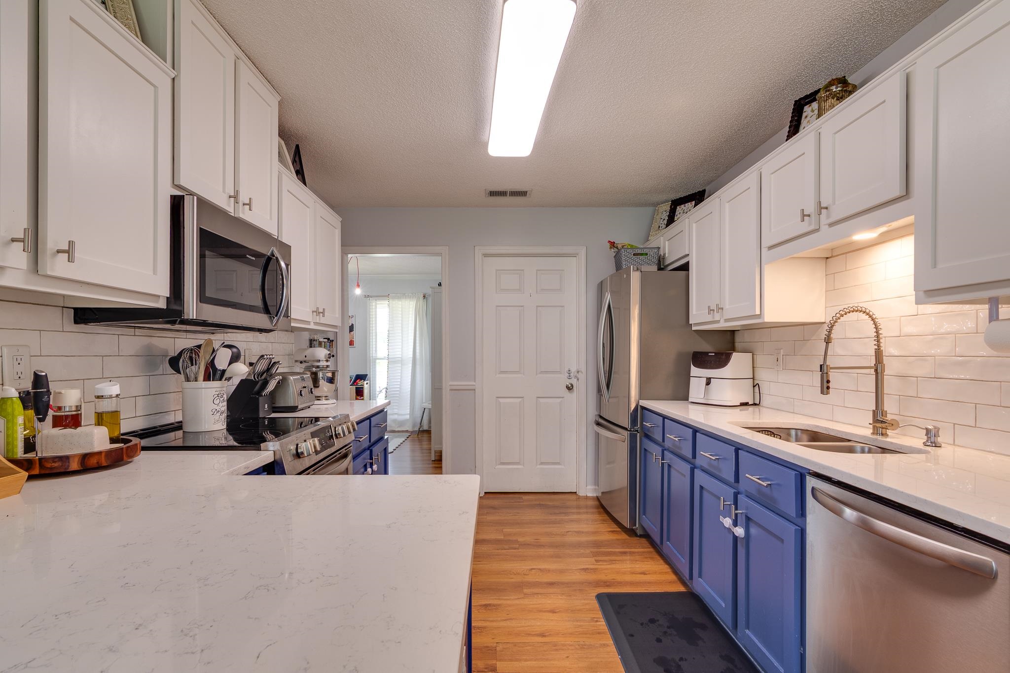 8703 Old River Road Memphis, TN 38018 - Photo 11 of 31 Kitchen featuring stainless steel appliances, blue cabinetry, white cabinets, backsplash, and a textured ceiling