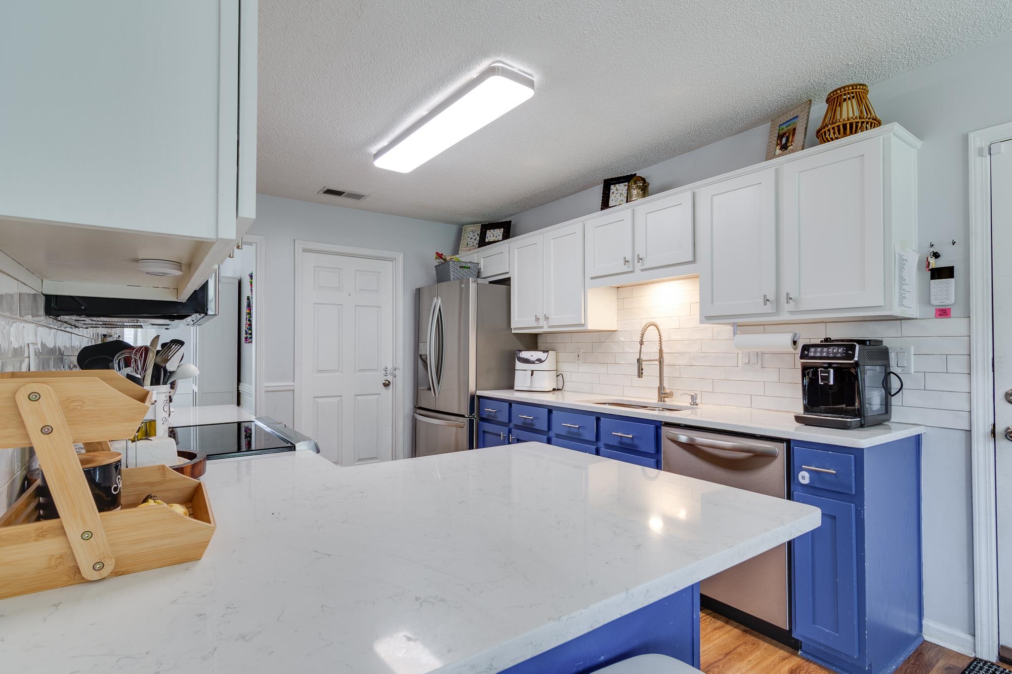 8703 Old River Road Memphis, TN 38018 - Photo 12 of 31 Kitchen featuring blue cabinetry, stainless steel appliances, tasteful backsplash, white cabinetry, and a textured ceiling