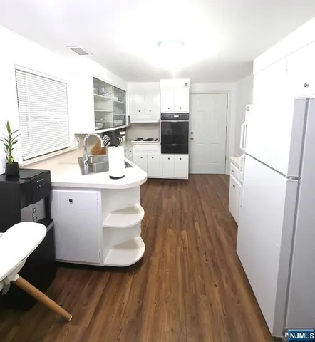 a kitchen with a sink a refrigerator a stove and white cabinets with wooden floor
