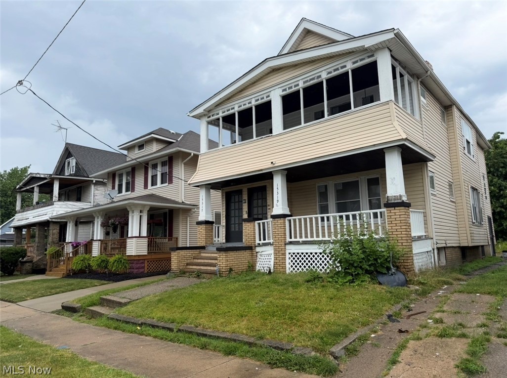 Multi-story residence featuring light-colored siding and a covered front porch with brick and white column supports