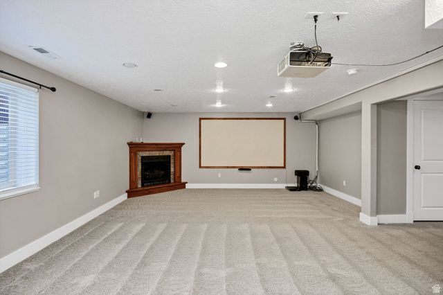 2912 South 1080th Street West Logan, UT 84321 - Photo 18 of 43 Spacious room featuring a corner fireplace with a detailed wood mantel, a large projection screen with wood trim, ceiling-mounted projector, recessed lighting, and light-toned carpet flooring