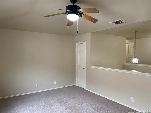 an empty room with a chandelier fan and wooden floor
