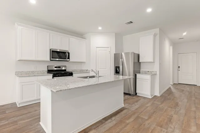 a kitchen with refrigerator a microwave a stove and white cabinets with wooden floor