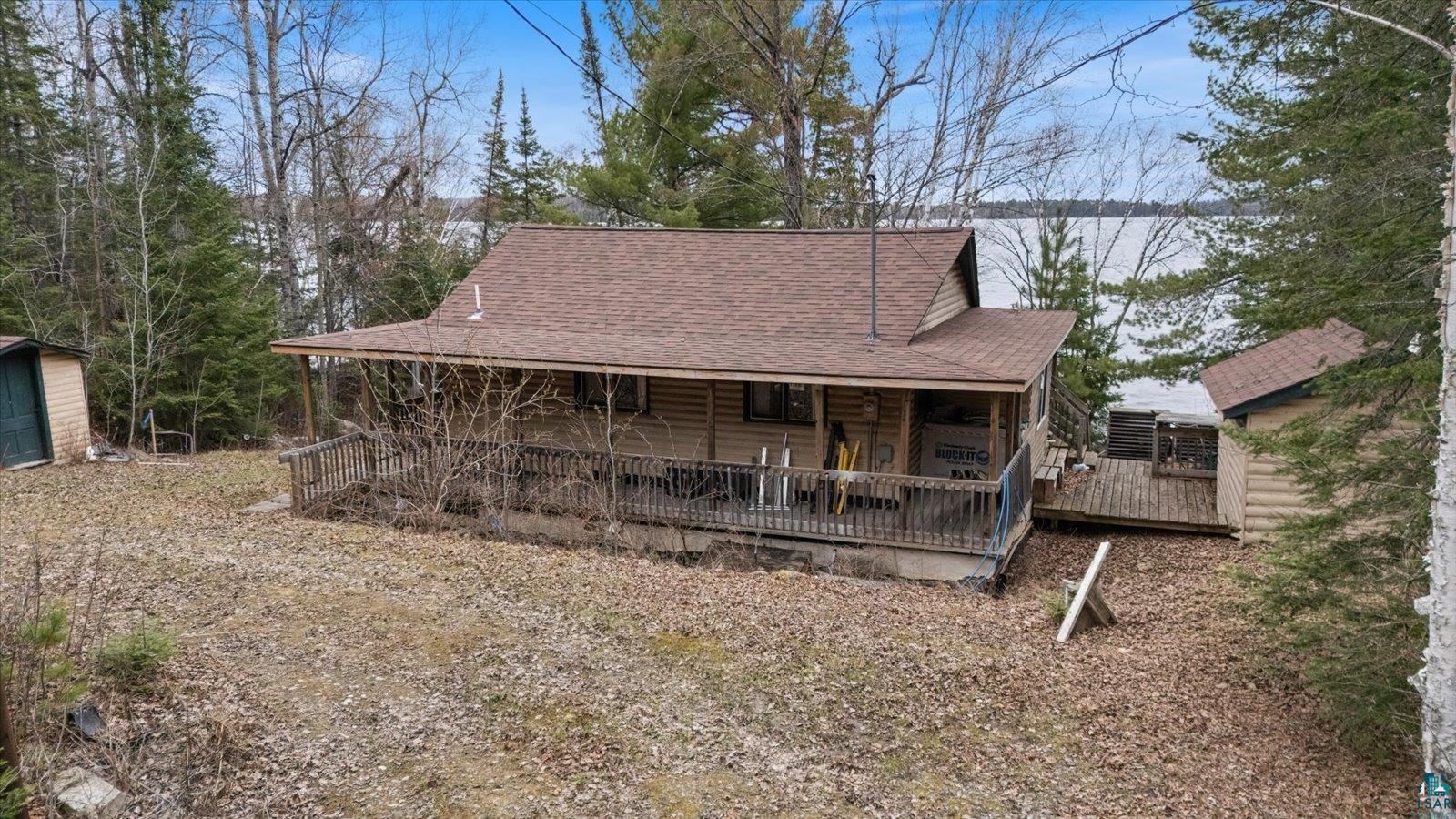Wood-sided cabin with a brown shingle roof and a covered front porch featuring a wood railing