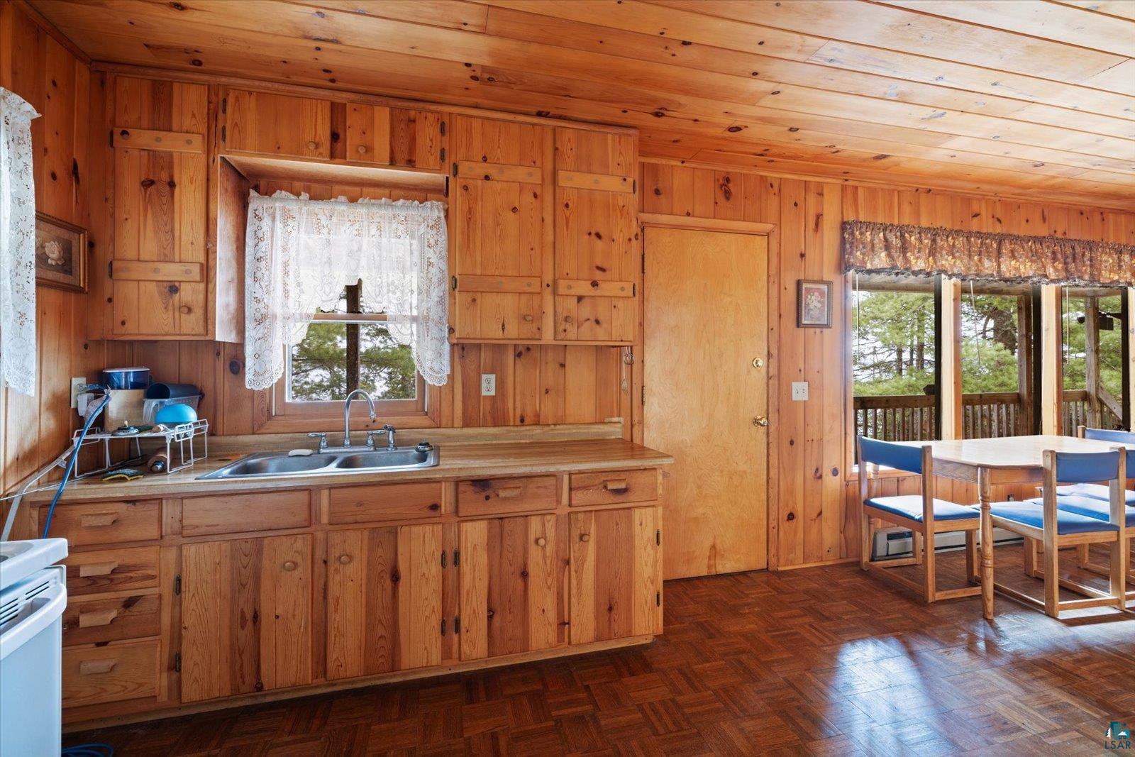 2014 West Frazer Bay Road Cook, MN 55723 - Photo 2 of 26 Wood-paneled interior featuring extensive cabinetry, a stainless steel double sink, wood-finish flooring, a full-light door, and large windows overlooking exterior decking