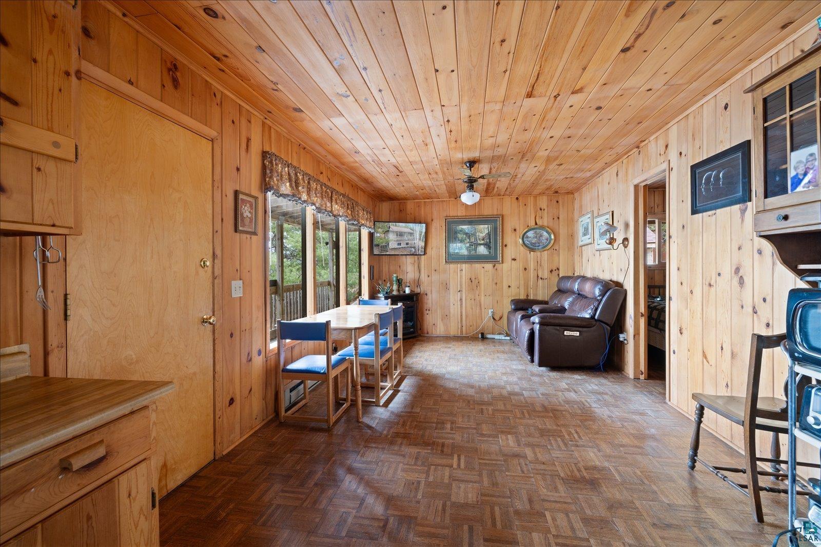 2014 West Frazer Bay Road Cook, MN 55723 - Photo 3 of 26 Open-concept living space featuring wood-paneled walls and ceiling, parquet wood-finish flooring, a dining area with multiple windows, and a ceiling fan