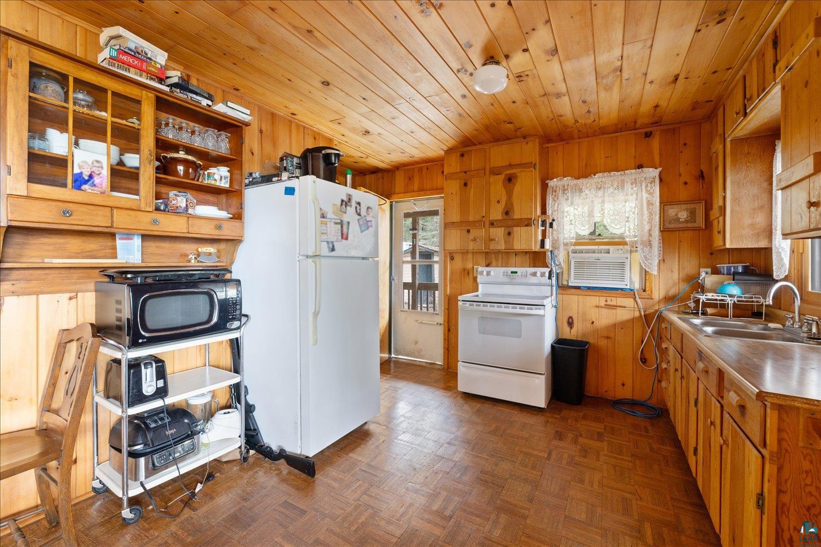 2014 West Frazer Bay Road Cook, MN 55723 - Photo 8 of 26 Kitchen featuring wood-paneled walls and ceiling, wood-finish flooring, white appliances, and a built-in wood hutch with glass-front cabinetry